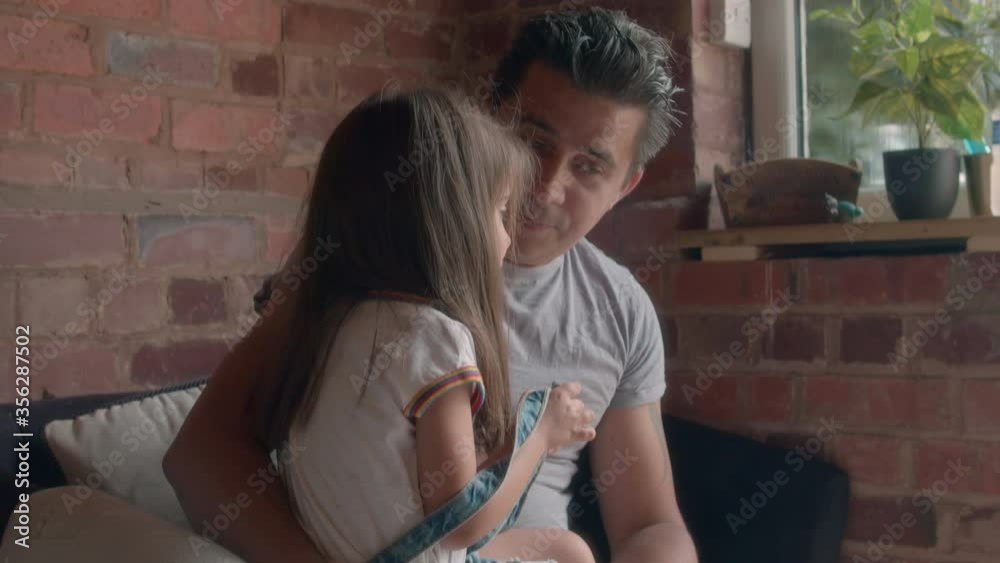 Father sitting indoors with his young daughter on his lap.