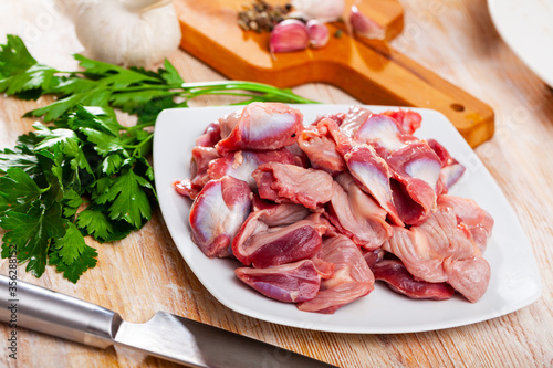 Raw chicken gizzards and greens on wooden surface