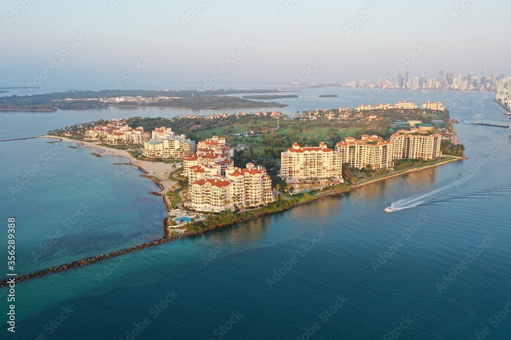 Aerial view of Fisher Island and Government Cut with City of Miami skyline and Port Miami in background at sunrise.