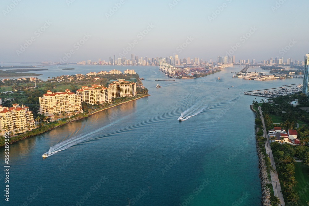 Obraz premium Aerial view of Fisher Island, South Pointe and Government Cut with City of Miami skyline and Port Miami in background at sunrise.