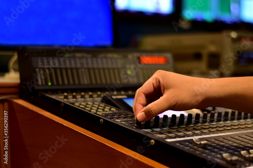 Closeup of sound engineer's hand moving sliders on audio mixing board.