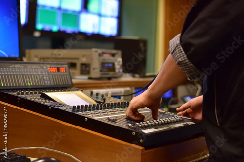 Closeup of sound engineer's hand moving sliders on audio mixing board.