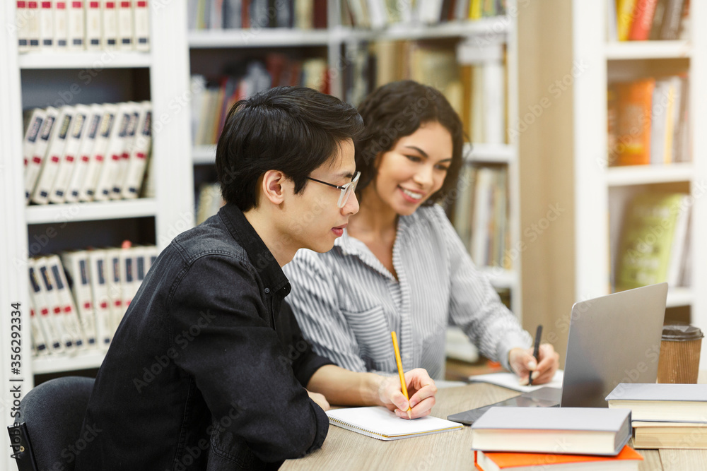 Two smiling multicultural students learning at public library Two smiling multicultural students learning at public library