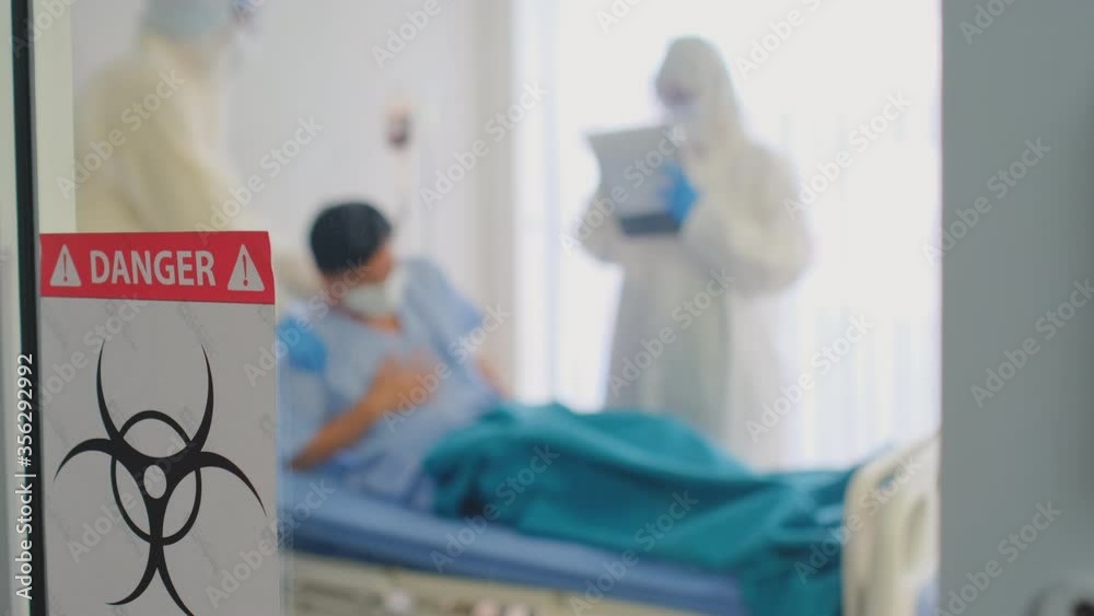 Main focus on biohazard banner with background of doctor and nurse team help to treatment patient in close room or high protective quarantine room to prevent spreading of covid virus during pandemic. Main focus on biohazard banner with background of doctor and nurse team help to treatment patient in close room or high protective quarantine room to prevent spreading of covid virus during pandemic.