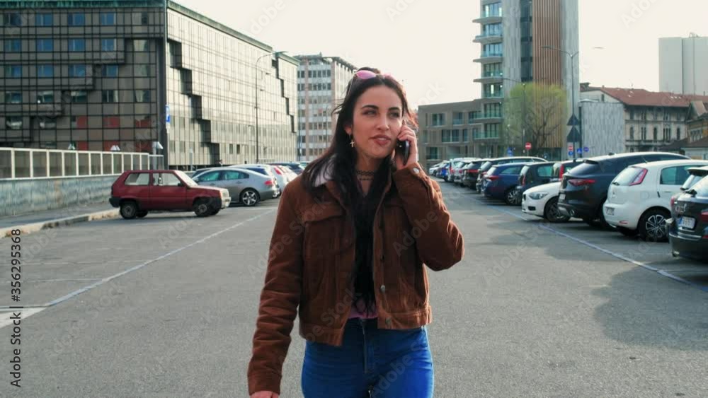 Girl walking through a car lot using her phone, making a call, Girl walking through a car lot using her phone, making a call,