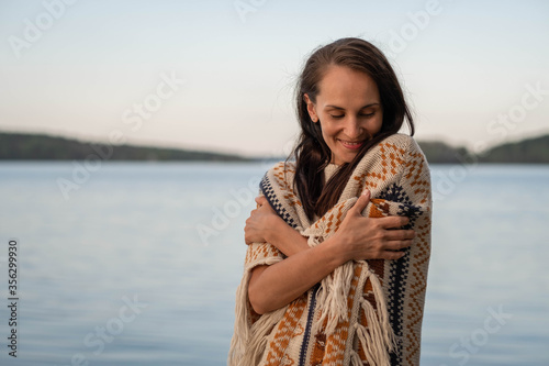 Stylish charming woman in a knitted poncho covers herself with her hands basking in the warmth of her clothes