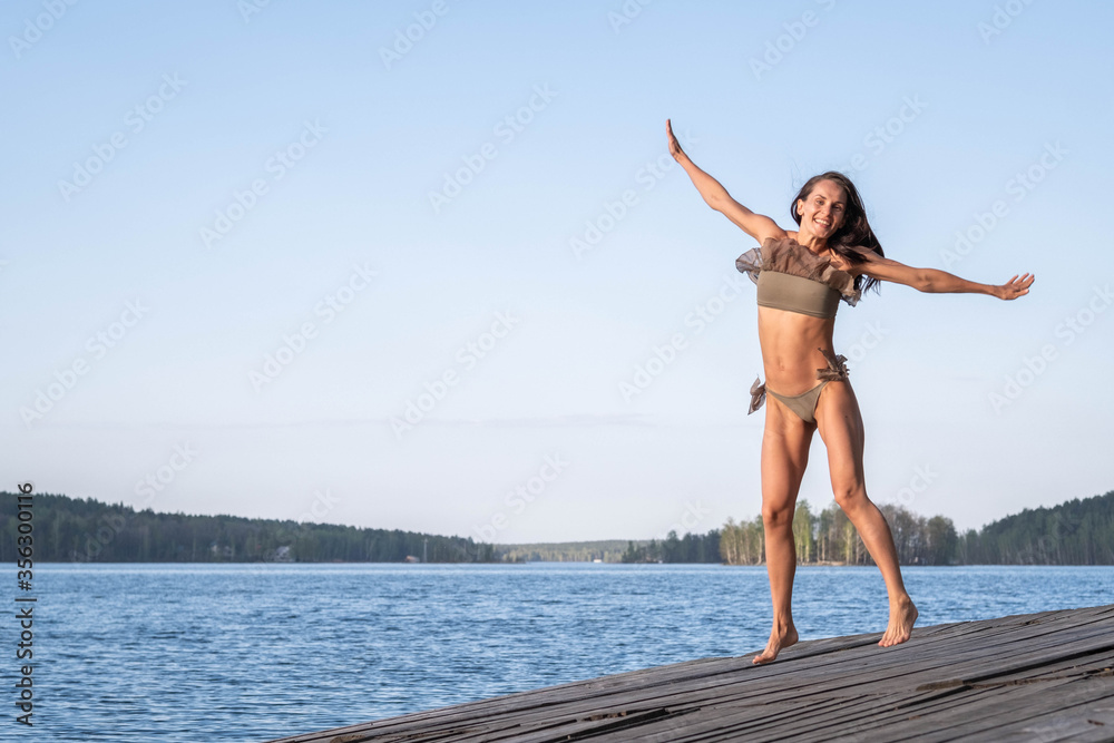 Naklejka premium A slender beautiful woman is happy to jump up on the pier in the hot summer