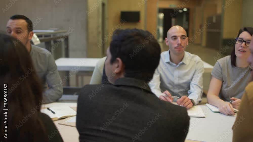 Panning shot of a group of people seated at a table, men and women