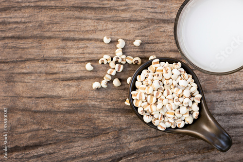 Closeup white Job's tears ( Adlay millet or pearl millet ) in black ceramic bowl and glass of millet milk isolated on wood table background ,Top view. Flat lay. photo