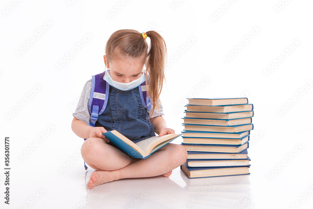 a first-grader learns to read. a little girl on home distance learning. A child in a medical mask reads a book. the student is doing homework. isolated on a white background a first-grader learns to read. a little girl on home distance learning. A child in a medical mask reads a book. the student is doing homework. isolated on a white background