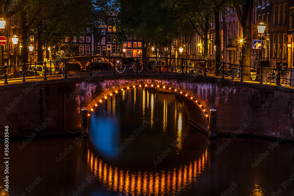 Illuminated bridge at twilight along a canal in Amsterdam