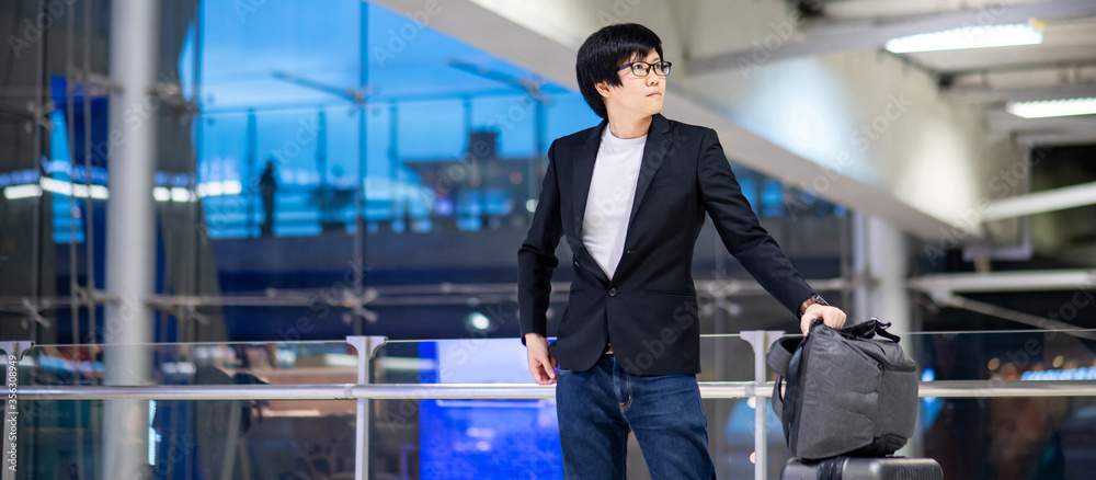 Business travel and baggage claim check-in concept. Smart Asian businessman wearing formal suit jacket carrying suitcase luggage and backpack waiting for the flight in international airport terminal. Business travel and baggage claim check-in concept. Smart Asian businessman wearing formal suit jacket carrying suitcase luggage and backpack waiting for the flight in international airport terminal.