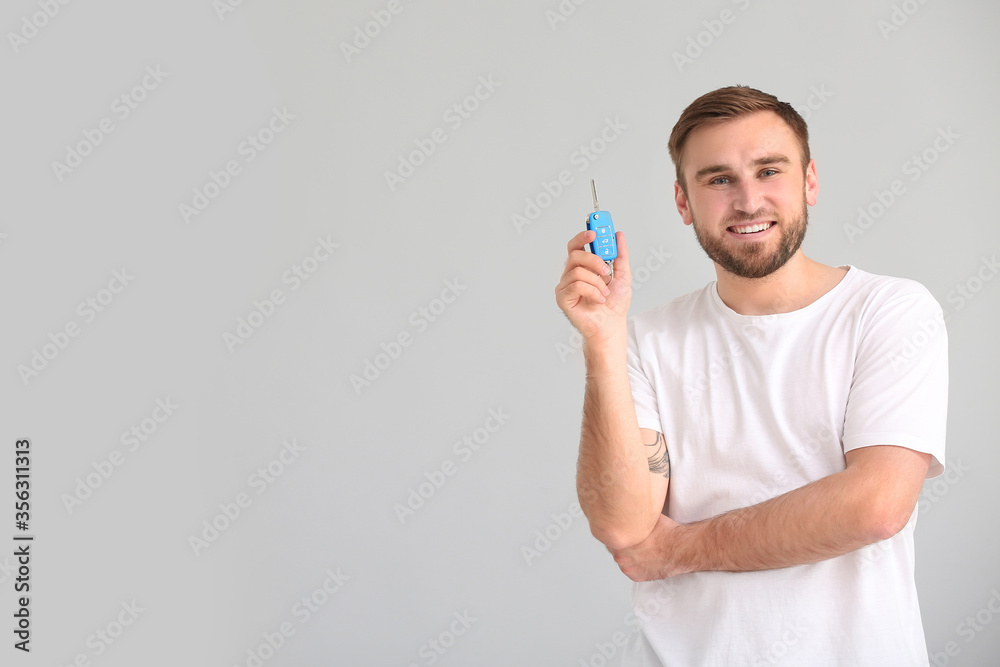 Young man with car key on grey background Young man with car key on grey background