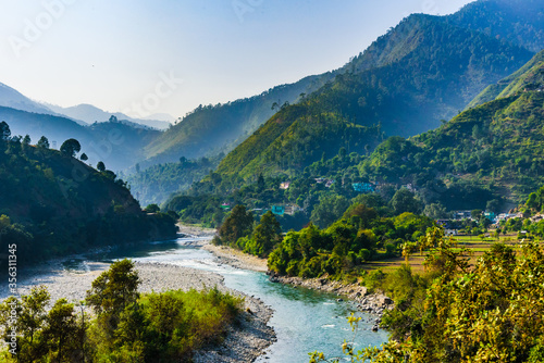 View of Ramganga river and the valley to the village and fields on the background of blue mountain ranges of the Himalayas, near Nainital, Uttarakhand, India.