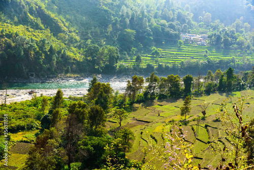 View of Ramganga river and the valley to the village and terrace fields on the background of blue mountain ranges of the Himalayas, near Nainital, Uttarakhand, India.