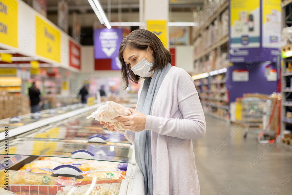 Woman wearing face mask buying in supermarket.Panic shopping during Coronavirus covid-19 pandemic. Budget buying at a supply store. Buying freezer smart purchased household pantry groceries