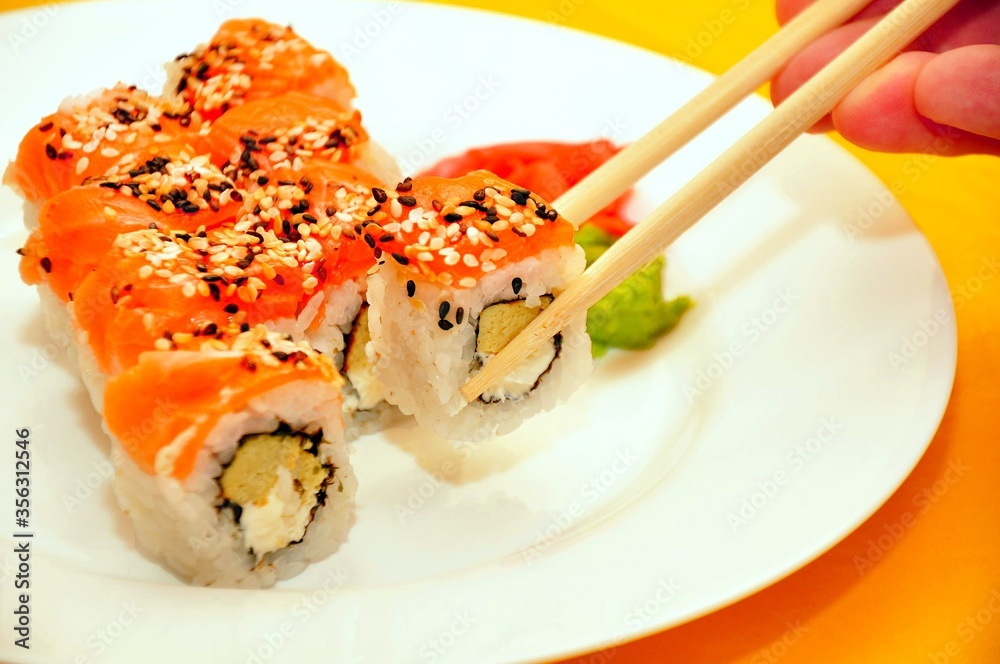 Colorful Sushi on white plate. Red sushi roll with rice salmon fish sesame black & white seeds wasabi sauce man eating in sushi bar. Sushi menu. Japanese delicious nigiri fish food. Seafood restaurant Colorful Sushi on white plate. Red sushi roll with rice salmon fish sesame black & white seeds wasabi sauce man eating in sushi bar. Sushi menu. Japanese delicious nigiri fish food. Seafood restaurant