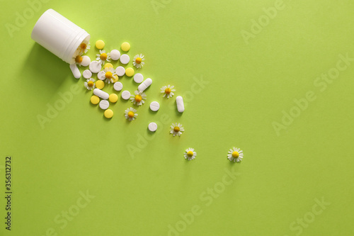 Pills with chamomile flowers on color background