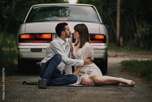 A guy and a girl are sitting in front of a car at sunset. Romantic date. © jen2215