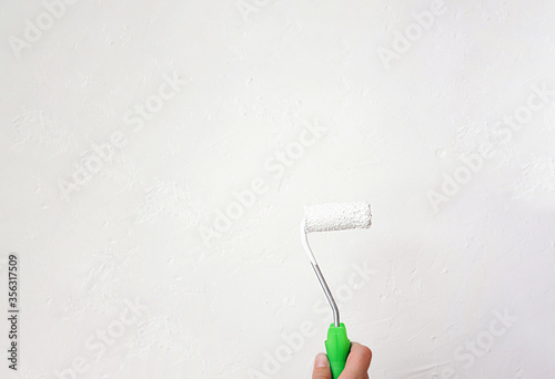 small roller in white paint with a bright green handle in a light skinned hand against a light gray concrete surface