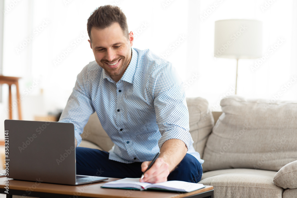Man using laptop at home and writing notes Man using laptop at home and writing notes