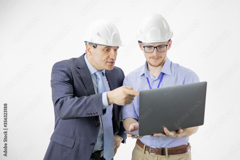 Two engineers in hard hats discuss new project while using laptop, making calculated engineering decisions isolated on white background. Team discussion. BIM, Industry construction Two engineers in hard hats discuss new project while using laptop, making calculated engineering decisions isolated on white background. Team discussion. BIM, Industry construction