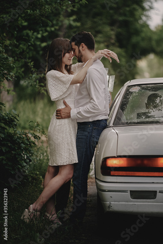 A guy and a girl are hugging next to a car. Romantic date evening walk. The relationship between people is love and tenderness. © ssergiocom