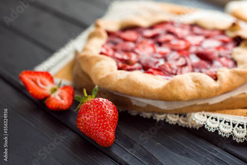 Close-up view of fresh strawberry on wooden black table on a background of baked pie with berries. Delicious traditional homemade pie. Housework. Copyspace. Flat lay. Daylight