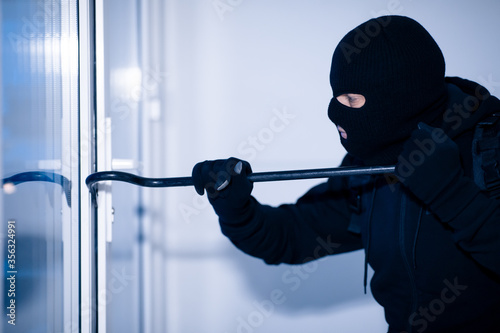 Valokuvatapetti Robber in black balaclava cracking door with crowbar