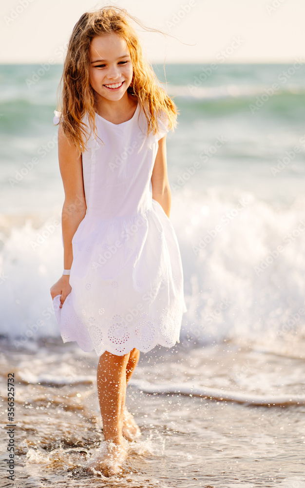 girl in white dress walks and fun on sea shore with big waves and strong winds.