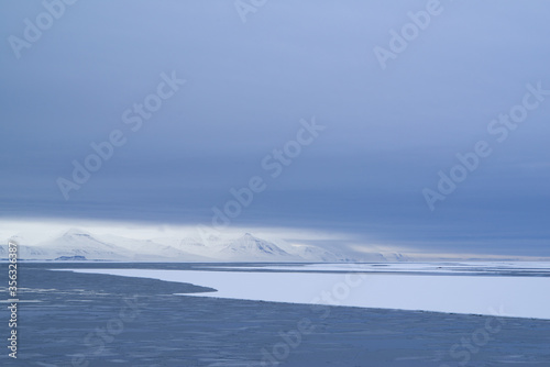 Melting sea ice in the Arctic on Spitsbergen. Mountains and clouds in white and blue at the horizon.