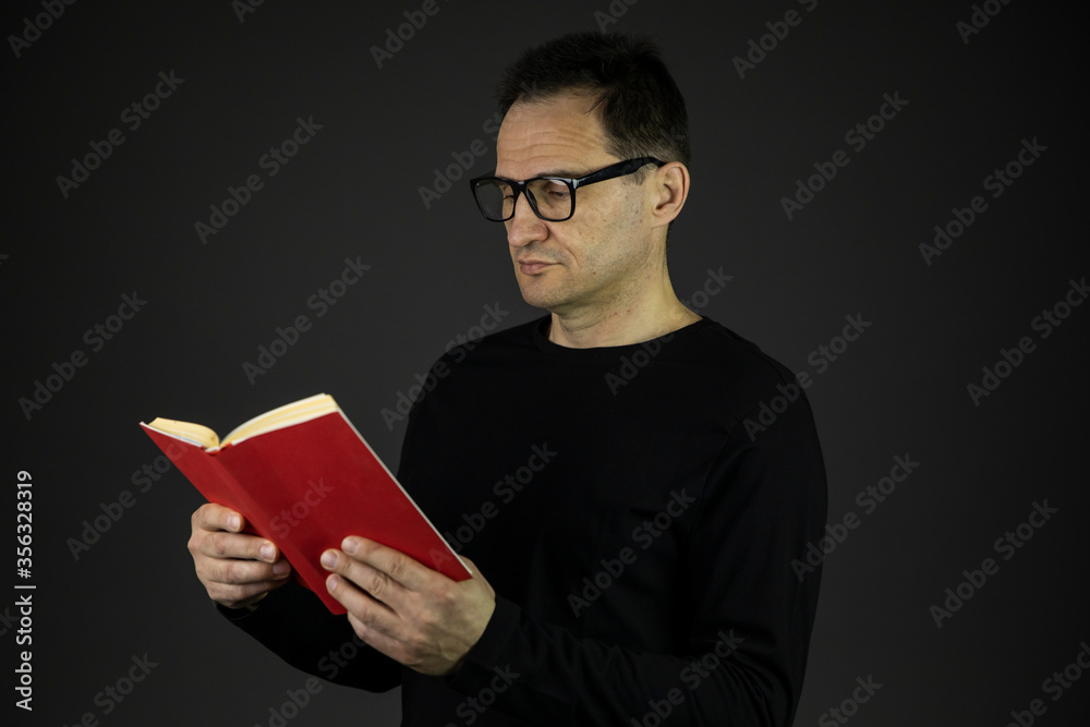 Smart senior age intelligent man in casual black wear and glasses reading interesting book isolated on dark background. Book lover, education, relaxing concept Smart senior age intelligent man in casual black wear and glasses reading interesting book isolated on dark background. Book lover, education, relaxing concept