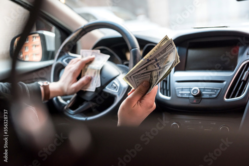 man in car holding dollar for bribe or pay in goods