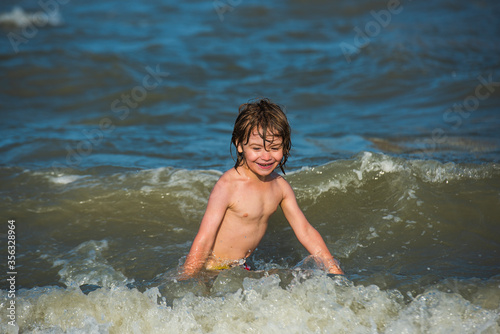 Summer kids vacation and healthy lifestyle concept. Little boy in the spray of waves at sea on a sunny day.