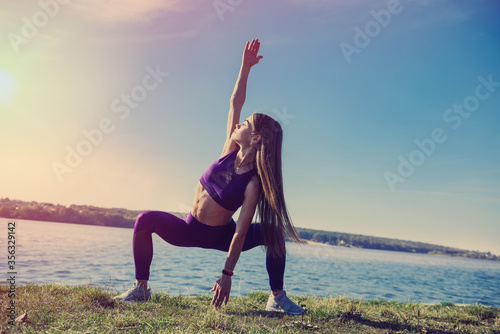 Young brunette woman in sportswear doing stretching her legs after the workout on the lake near daytime. Healthy lifestyle.