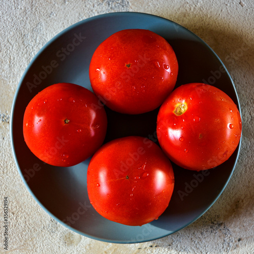 Four red ripe tomatoes on a blue plate. Close-up. View from above.