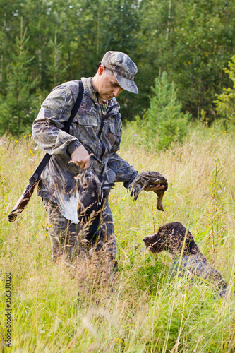 a hunter takes a downed grouse from a dog photo