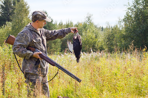 the hunter holds the shotgun in one hand and the down game in the other hand