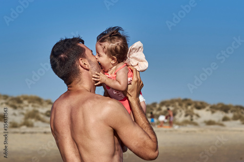 father holds her little child on hands on the beach on a sunny spring day