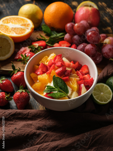 Dessert salad with sour cream and summer fruits mix in bowl on table background with ingredients