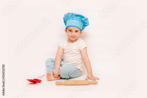 A little boy in a chef's hat cooks in a toy kitchen on a white background
