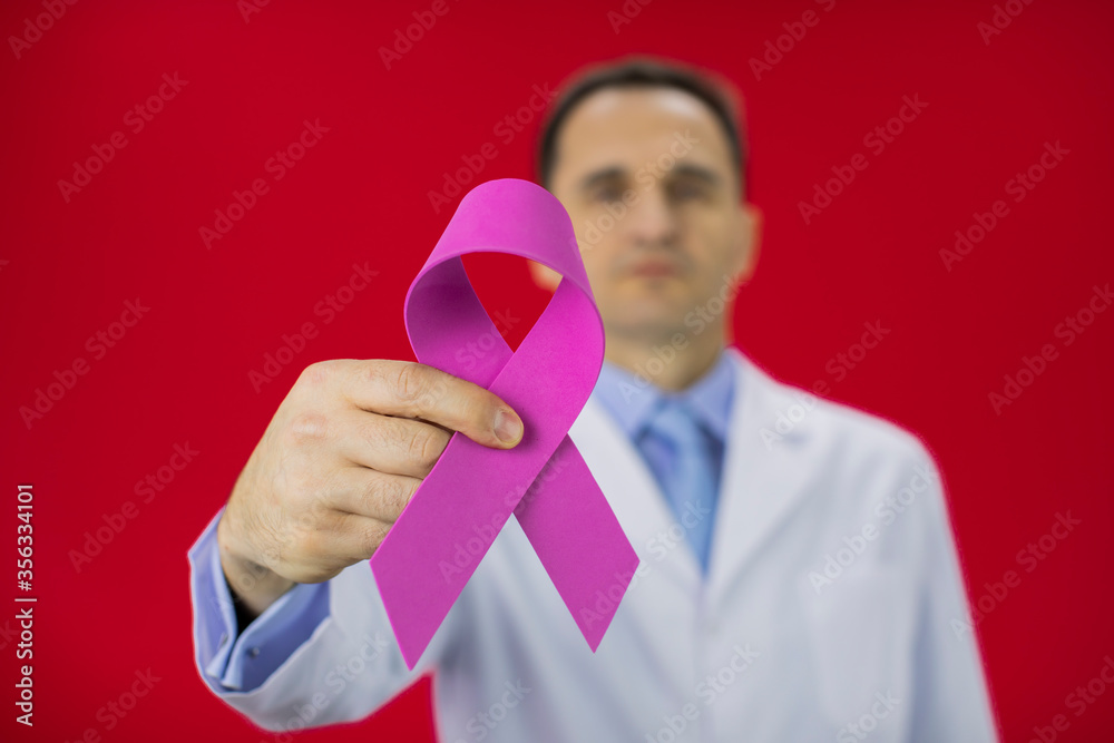 Handsome serious male senior age doctor in white lab coat with pink ribbon in hand on red background. Focus on ribbon, Breast thyroid cancer awareness campaigns, symbol of october, medical sign Handsome serious male senior age doctor in white lab coat with pink ribbon in hand on red background. Focus on ribbon, Breast thyroid cancer awareness campaigns, symbol of october, medical sign