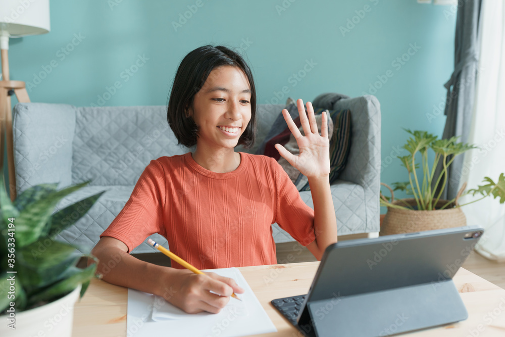 Happy Asian girl is study online via internet on tablet waving in greeting Happy Asian girl is study online via internet on tablet waving in greeting