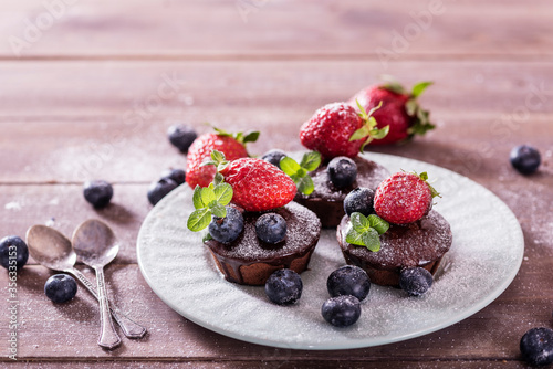 Chocolate cakes (cupcakes) are on the table. Cupcakes decorated  blueberries, strawberries and green leaves mint on top. Beautiful and elegant serving with white dishes