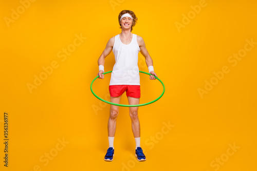 Full length body size view of nice funky slim thin cheerful cheery glad motivated guy spinning plastic circle around waist isolated over bright vivid shine vibrant yellow color background © deagreez