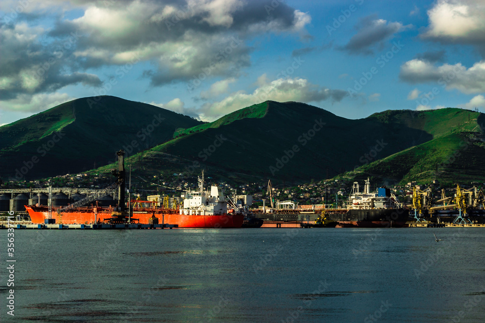 Sea ships stand in port of Novorossiysk at sunny day. Sea ships and the mountains.