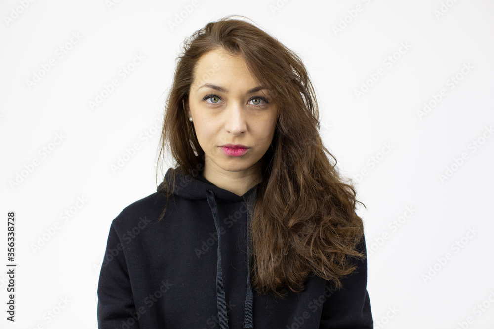 Portrait of young beautiful serious woman with long dark curly hair wearing black hoodie looking at camera isolated on white background Portrait of young beautiful serious woman with long dark curly hair wearing black hoodie looking at camera isolated on white background