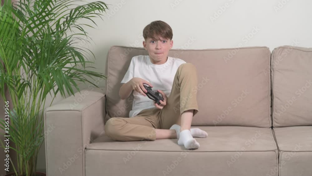 Boy plays video games while sitting on the couch with a joystick in his hands. Boy plays video games while sitting on the couch with a joystick in his hands.