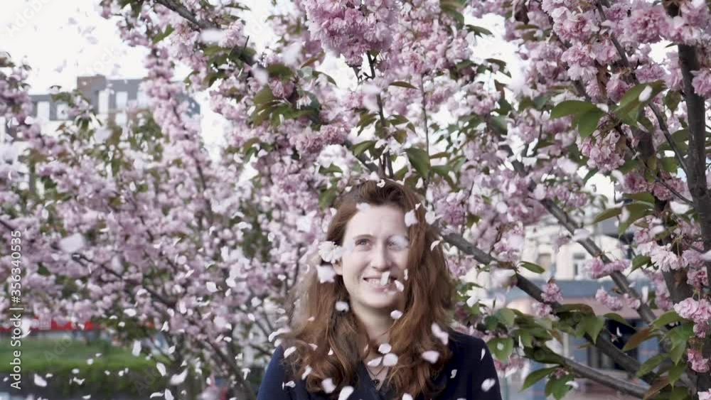 Young red-haired girl blowing pink petals of sakura tree in the park. Mid-range slow motion Full HD Young red-haired girl blowing pink petals of sakura tree in the park. Mid-range slow motion Full HD
