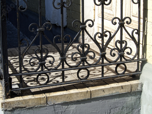 Figured metal fence illuminated by sunlight in front of the old entrance double-pane paneled door